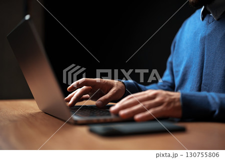 Individual typing on laptop during late evening at a wooden desk with dark background Individual typing on laptop during late evening at a wooden desk with dark background 130755806