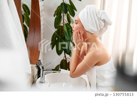 Woman applying facial skincare in a serene bathroom with plants and natural light in the early morning 130755813