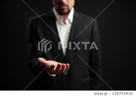 Businessman presenting an open hand against a dark background showcasing an invitation or offer 130755910