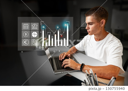 Young man analyzes financial data on a laptop in a modern office setting during daytime hours 130755940