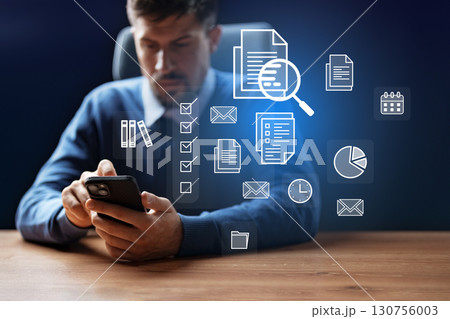 Professional analyzing documents while using smartphone in a modern office setting during daylight hours 130756003