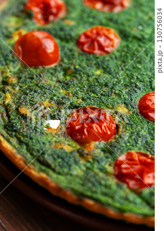 Spinach and tomato flatbread baked in a rustic kitchen highlighting vibrant colors and fresh ingredients during afternoon light 130756034