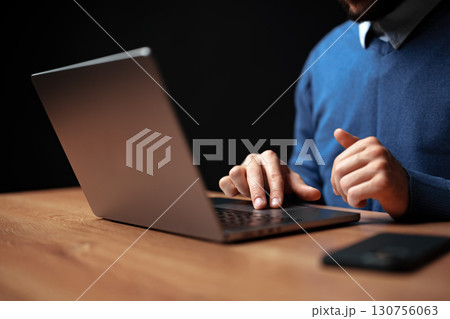 Engaging in focused work on a sleek laptop at a wooden desk in a modern indoor space 130756063