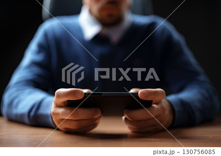Individual engaging in mobile gaming while seated at a desk in a dimly lit environment Individual engaging in mobile gaming while seated at a desk in a dimly lit environment 130756085