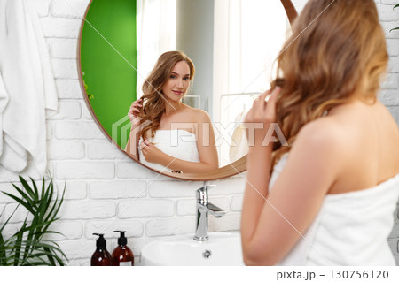 Woman preparing her hair in a bright bathroom with modern decor and natural light streaming through the window 130756120