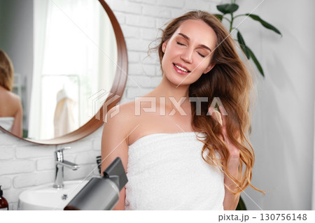 Woman preparing her hair in a bright bathroom with modern decor and natural light streaming through the window Woman preparing her hair in a bright bathroom with modern decor and natural light streaming through the window 130756148