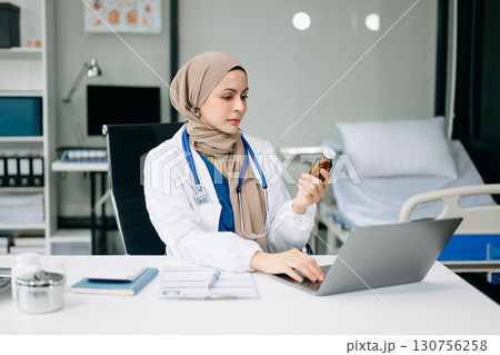 Beautiful physician doctor sit on table in office hospital. Attractive therapist female practitioner pharmacist smile and use tablet and laptop. Beautiful physician doctor sit on table in office hospital. Attractive therapist female practitioner pharmacist smile and use tablet and laptop. 130756258