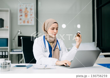 Young Doctor in medical uniform with stethoscope using computer laptop and tabler talking video conference call with patient at desk in health clinic or hospital. Young Doctor in medical uniform with stethoscope using computer laptop and tabler talking video conference call with patient at desk in health clinic or hospital. 130756259
