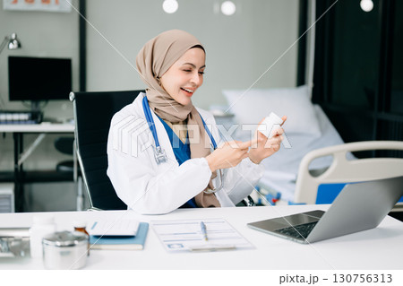 Young Doctor in medical uniform with stethoscope using computer laptop and tabler talking video conference call with patient at desk in health clinic or hospital. Young Doctor in medical uniform with stethoscope using computer laptop and tabler talking video conference call with patient at desk in health clinic or hospital. 130756313