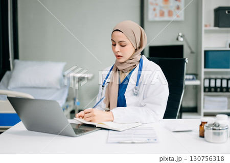 Beautiful physician doctor sit on table in office hospital. Attractive therapist female practitioner pharmacist smile and use tablet and laptop. Beautiful physician doctor sit on table in office hospital. Attractive therapist female practitioner pharmacist smile and use tablet and laptop. 130756318