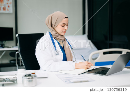 Beautiful physician doctor sit on table in office hospital. Attractive therapist female practitioner pharmacist smile and use tablet and laptop. Beautiful physician doctor sit on table in office hospital. Attractive therapist female practitioner pharmacist smile and use tablet and laptop. 130756319