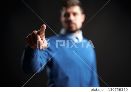 Person in blue sweater pointing with finger in dramatic lighting against black background Person in blue sweater pointing with finger in dramatic lighting against black background 130756350