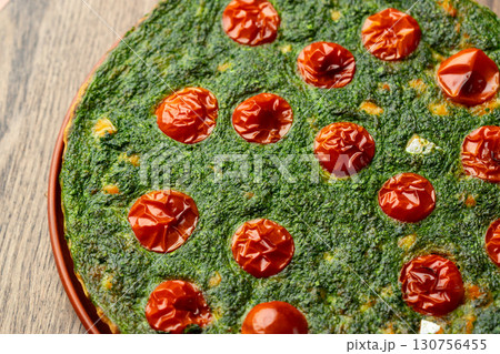 Savory spinach tart with roasted tomatoes on wooden table under warm light 130756455