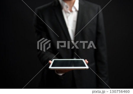 Business professional presenting a tablet in a dark setting with a focus on technology and communication Business professional presenting a tablet in a dark setting with a focus on technology and communication 130756460
