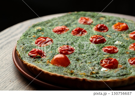 Freshly baked savory tart featuring vibrant spinach and sun-dried tomatoes on a wooden table at a cozy kitchen 130756687