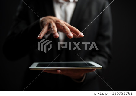Professional man using tablet with fingers hovering over screen in dark background 130756762
