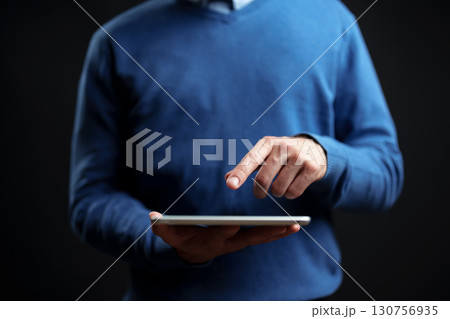 Person using a tablet while wearing a blue sweater in a dark setting 130756935