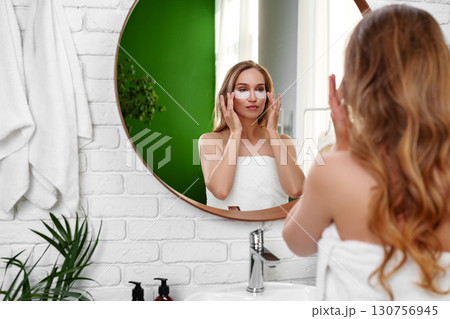 Woman applying face mask while looking in mirror at home bathroom during morning routine Woman applying face mask while looking in mirror at home bathroom during morning routine 130756945