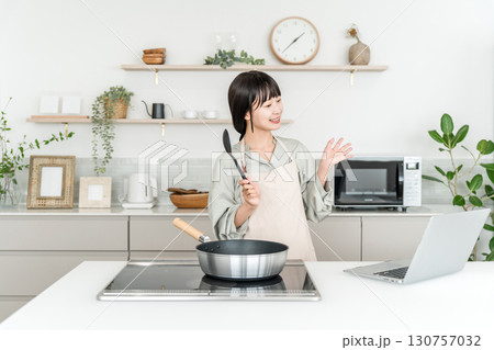 キッチンでパソコンを見ながら料理をする若いアジア人女性 キッチンでパソコンを見ながら料理をする若いアジア人女性 130757032