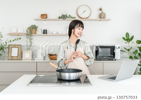 キッチンでパソコンを見ながら料理をする若いアジア人女性 130757033