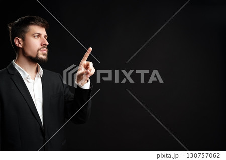 Professional man points up while wearing a black suit against a dark background during a corporate presentation 130757062