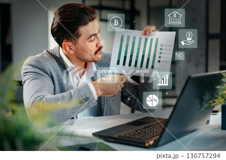 Business professional analyzing financial charts in a modern office setting during the day 130757294