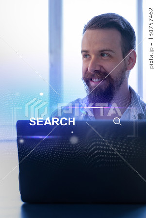 Smiling man engaged in online search activity at a bright office space during daytime 130757462