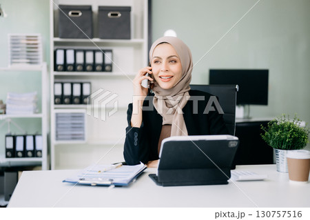 Young Arabic female entrepreneur wearing a hijab working  with a laptop Concentrated math finance on an office 130757516
