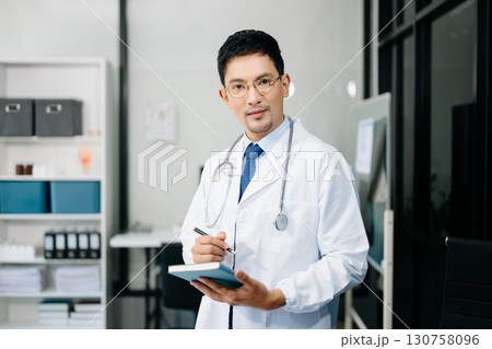 Physician doctor sit on table in office hospital. Attractive therapist male practitioner pharmacist smile and use tablet and laptop. 130758096