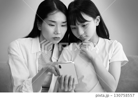 スマホを真剣に見る母と娘のイメージ スマホを真剣に見る母と娘のイメージ 130758557