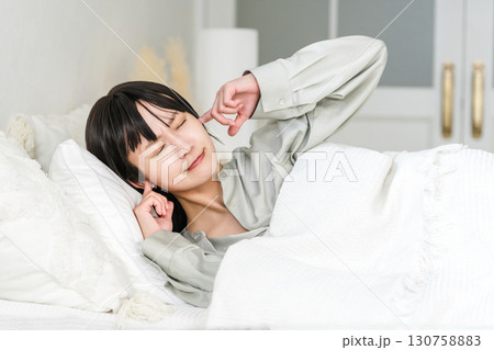 ベッドで睡眠中に騒音で耳を塞ぐ若いアジア人女性（騒音トラブル,安眠妨害,睡眠障害） 130758883