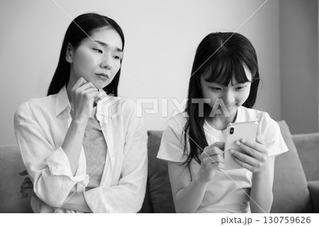 スマホに夢中になる娘を心配する母親のイメージ スマホに夢中になる娘を心配する母親のイメージ 130759626