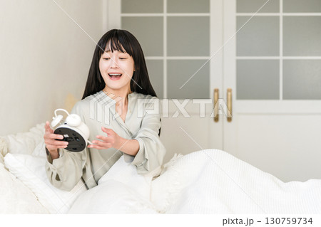目覚まし時計を見て驚くびっくりする若いアジア人女性（寝坊,遅刻,寝過ごす） 130759734