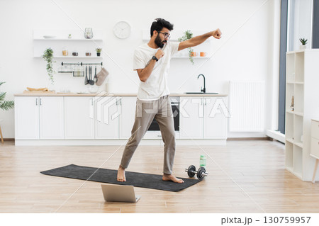 Man in 30s practicing boxing exercises in spacious kitchen on yoga mat, showing fitness. 130759957