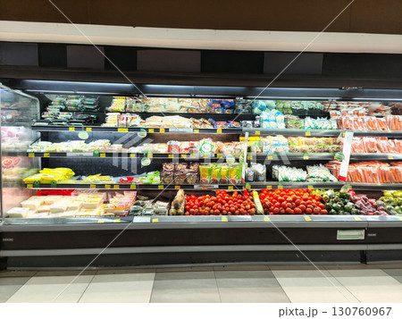 Descriptions A wide-angle shot of a refrigerated grocery store display case featuring a variety of packaged and fresh food items, including vegetables like tomatoes and avocados. 130760967