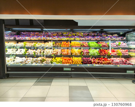Descriptions A wide-angle shot of a refrigerated grocery store display case featuring a variety of packaged and fresh food items, including vegetables like tomatoes and avocados. 130760968