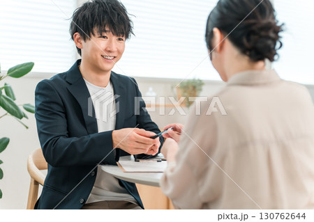商談テーブルで女性顧客と打ち合わせ,カウンセリング,ヒアリングをする若いアジア人ビジネスマン 130762644