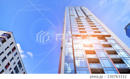 Exterior of a high modern multi-story apartment building - facade, windows and balconies. Timeless glass facade. Modern urban living district. Exterior of a high modern multi-story apartment building - facade, windows and balconies. Timeless glass facade. Modern urban living district. 130763332