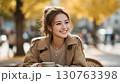 秋の街並みでコーヒーを楽しむ笑顔の女性 130763398
