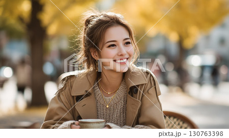 秋の街並みでコーヒーを楽しむ笑顔の女性 130763398