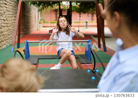 Young Girl Playing Happily on a Playground Seesaw Outdoors 130763633