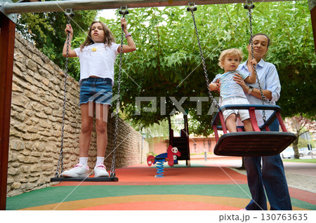 Mother and Children Enjoy Swing Time at an Outdoor Playground 130763635
