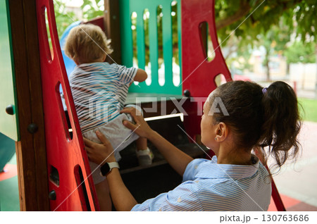 Mother Assisting Child Climb Playground Structure in Outdoor Park 130763686