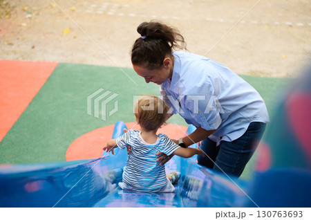 Mother Helping Child Slide on Playground for Fun and Adventure 130763693