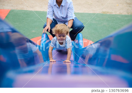 Child Climbing a Slide with Parental Support at Outdoor Playground 130763696