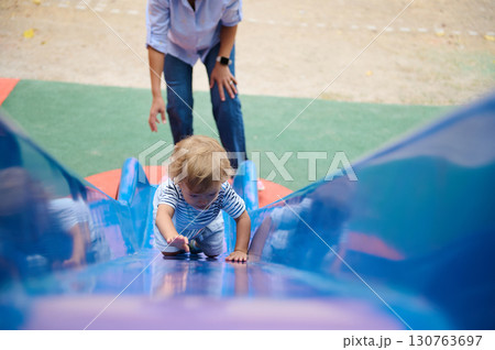 Child Climbing Slide with Parent Assistance at Outdoor Playground Child Climbing Slide with Parent Assistance at Outdoor Playground 130763697