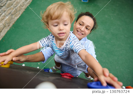 Mother Supporting Young Child Climbing Wall at Playground Mother Supporting Young Child Climbing Wall at Playground 130763724