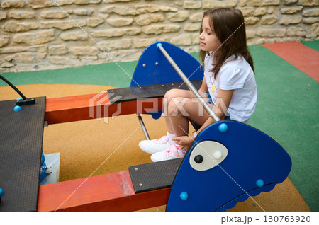 Young Girl Enjoying a Seesaw Ride in a Colorful Playground 130763920