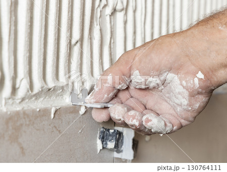 Craftsman hand place tile spacers during tiling a wall, closeup. Construction or rennovation of a house Craftsman hand place tile spacers during tiling a wall, closeup. Construction or rennovation of a house 130764111