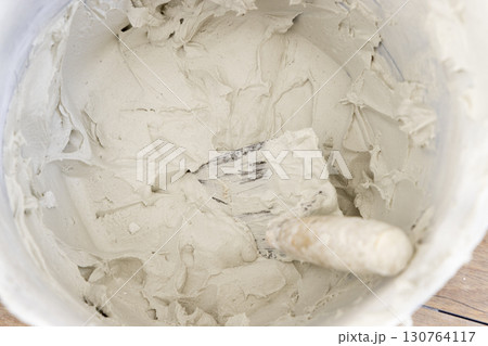 Bucket with grout or plaster with trowel inside, covered in cement residue, top view 130764117